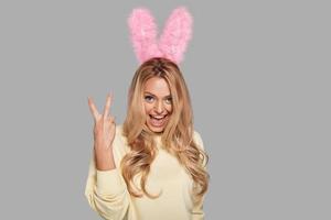 Staying cool. Attractive young smiling woman in pink bunny ears gesturing and looking at camera while standing against grey background photo