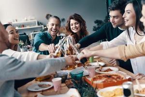 grupo de jóvenes con ropa informal recogiendo pizza y sonriendo mientras cenan en el interior foto