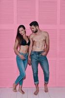 Simple joy of loving. Full length of beautiful young couple holding hands while standing against pink background photo