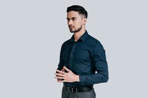 Thinking about solutions.  Handsome young man holding hands clasped and looking away while standing against grey background photo