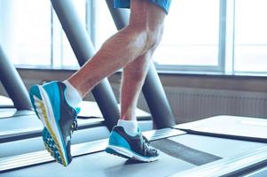 Run to success. Close-up part of man in sports shoes running on treadmill at gym photo