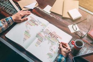 Planning global business ideas. Top view close-up image of man holding hands on his notebook with colorful map on it while sitting at the wooden desk photo