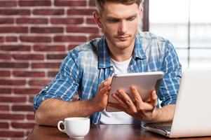 Examining his new gadget. Handsome young man working on digital tablet while sitting at the table photo