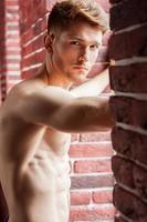 Feeling flirty. Handsome young shirtless man looking at camera while standing in front of the window photo