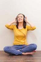 disolviéndose en una música encantadora. bella joven con auriculares manteniendo los ojos cerrados mientras se sienta en el suelo contra el fondo marrón foto