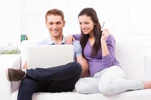 compras en línea juntos. hermosa joven pareja amorosa comprando en línea mientras se sientan juntos en el sofá foto