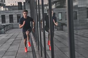 Keep running. Full length of young man in sports clothing running while exercising outside photo