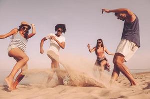 Spending great time with friends. Group of cheerful young people playing with soccer ball on the beach photo