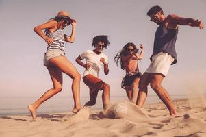 diversión en la playa grupo de jóvenes alegres jugando con una pelota de fútbol en la playa foto
