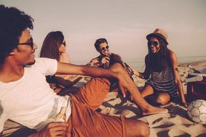 Beach party. Cheerful young people spending nice time together while sitting on the beach and drinking beer photo