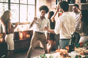 sigan bailando jóvenes alegres bailando y bebiendo mientras disfrutan de una fiesta en casa en la cocina foto