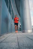 toda la longitud de un joven delgado con ropa deportiva trotando mientras hace ejercicio al aire libre foto