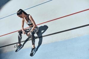 tomando tiempo para descansar. vista superior de una joven con ropa deportiva descansando mientras se sienta en la pista de atletismo al aire libre foto