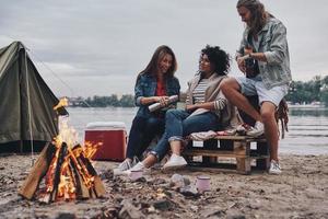 Warm and cozy. Group of young people in casual wear smiling while enjoying beach party near the campfire photo