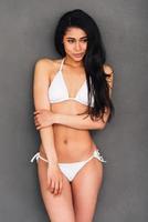 Flirty beauty. Beautiful young mixed race woman in white bikini posing against grey background and looking away photo