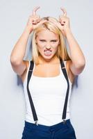 Beautiful devil. Beautiful young blond hair women making a face while standing against grey background photo