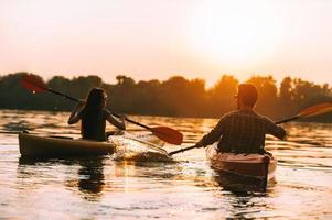 Meeting the best sunset together. Rear view of young couple kayaking on lake together with sunset in the backgrounds photo