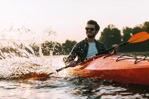 este es el apuesto joven sonriente de la vida real que salpica agua mientras navega en kayak por el río foto