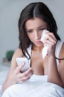 Women crying. Beautiful young women crying while looking at her mobile phone sitting in bed photo