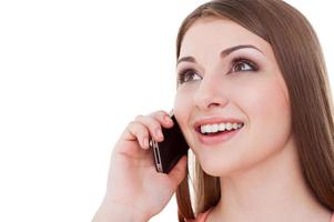 buena plática. mujer joven feliz hablando por teléfono móvil y sonriendo mientras está de pie aislado en blanco foto