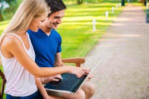 aprovechando las ventajas de la era digital. vista lateral de una hermosa joven pareja amorosa sentada en el banco juntos y mirando una laptop foto