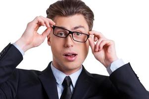 Businessman grimacing. Playful young man in formalwear adjusting his glasses and grimacing while looking at camera and standing isolated on white photo