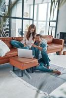 hermosa pareja joven usando laptop y sonriendo mientras pasa tiempo en casa foto