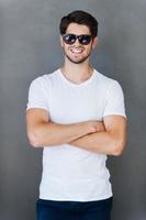 Casually handsome. Handsome young man keeping arms crossed and smiling while standing against grey background photo