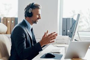 hombre de negocios feliz con auriculares que tiene una conferencia web mientras está sentado en su lugar de trabajo foto