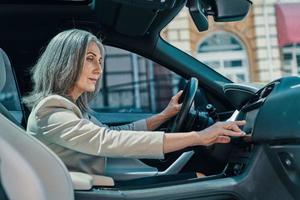 Mature beautiful woman in smart casual wear using global positioning system while driving car photo