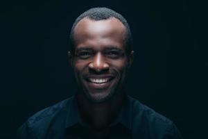 Cheerful young man. Portrait of handsome young African man looking at camera with smile while being in front of black background photo