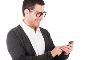 hombre escribiendo un mensaje. joven alegre sosteniendo un teléfono móvil y mirándolo mientras está aislado en blanco foto