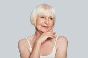 Aging process. Beautiful senior woman looking away and smiling while standing against grey background photo