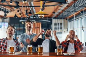 Cheering young men in casual clothing drinking beer and watching sport game photo