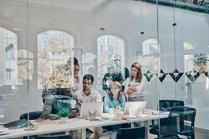 Group of young modern people in smart casual wear communicating and using modern technologies while working in the office photo