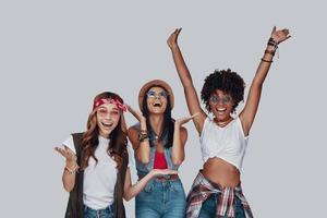 Three attractive young women cheering and smiling while standing against grey background photo