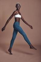 In her own style. Full length of attractive young African woman looking at camera and smiling while walking against brown background photo