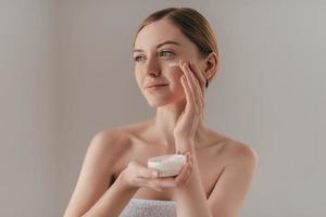 Taking good care of her skin. Gorgeous young woman looking away and smiling while standing against background photo