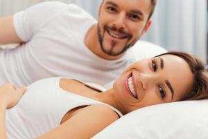 Waking up with smile. Beautiful young loving couple lying in bed together and smiling photo