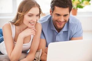 Spending their free time in the net. Cheerful young couple surfing the net together while lying on the floor and looking at the laptop photo