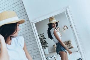 Looking just perfect. Attractive young woman looking at her reflection in the mirror while trying on her sun hat photo