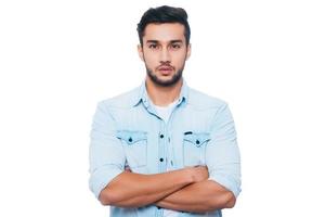 Portrait of confidence. Confident young Indian man keeping arms crossed and looking at camera while standing against white background photo