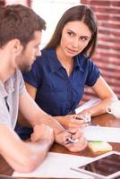 Discussing new business project. Side view of cheerful young man and woman sitting at the table and talking while man pointing digital tablet and smiling photo