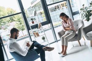 She needs help. Young frustrated woman solving her mental problems while sitting on the therapy session with psychologist photo