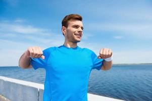 calentar antes de correr. apuesto joven haciendo ejercicio mientras está de pie al aire libre foto