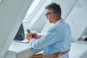 Confident mature man using mobile phone while sitting at the office desk photo