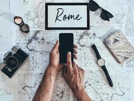 Roma. cerrar la vista superior del hombre usando un teléfono inteligente con gafas de sol, cámara fotográfica, brújula, reloj y pasaporte en el mapa alrededor foto