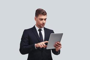 Achieving best results. Handsome young man using digital tablet while standing against grey background photo