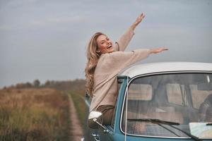 ¿Qué es la vida sin aventuras? Una joven atractiva que se asoma por la ventana de la furgoneta y sonríe mientras disfruta del viaje en coche con su novio. foto