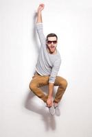 Just having fun. Excited young man jumping in front of the white wall and keeping mouth open photo